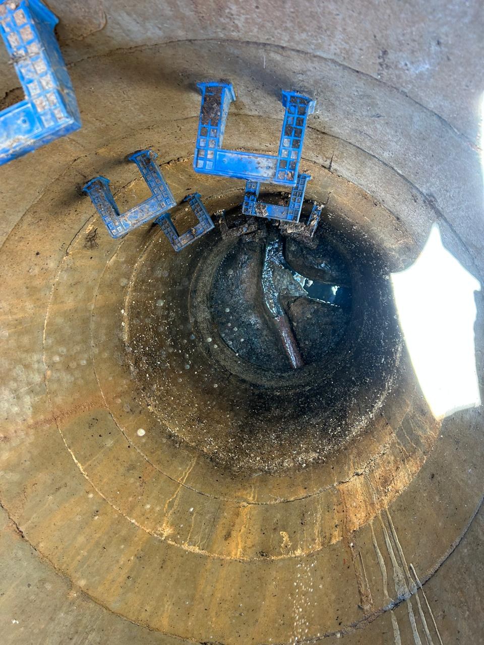 Inside a circular drain inspection chamber showing blue access steps and the drainage channel